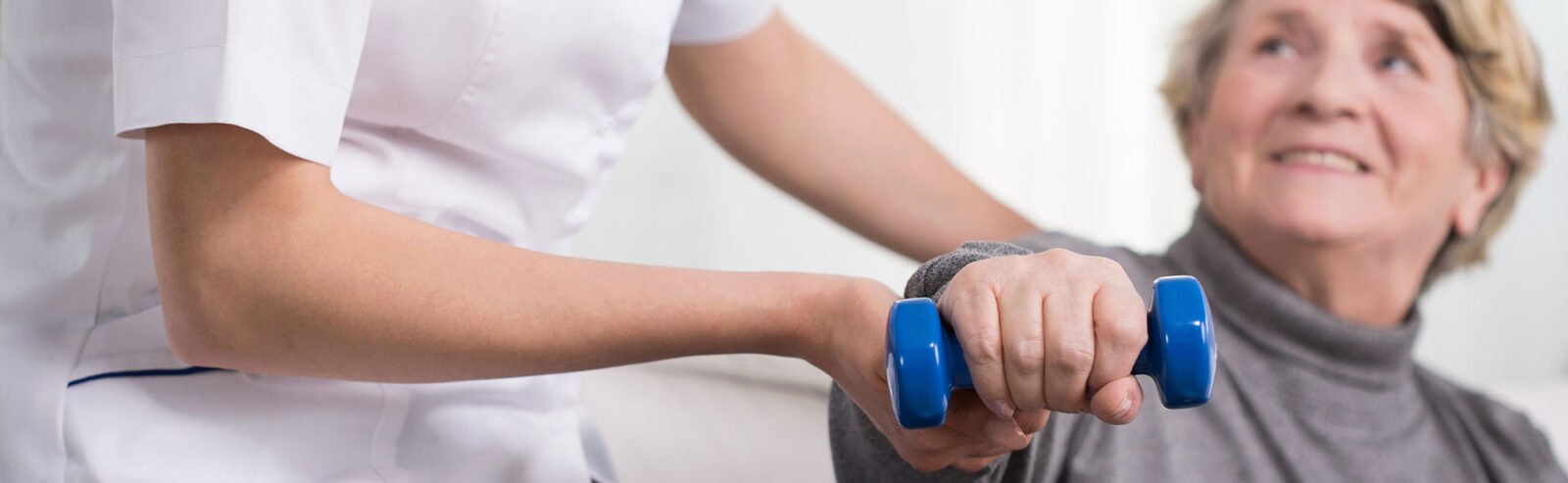 Elder woman training with dumbbell supported by physiotherapist